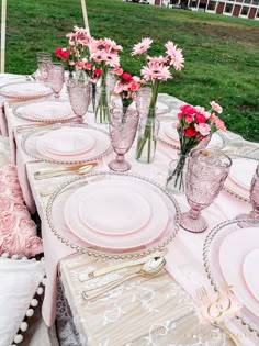 the table is set with pink and white plates, silverware, and vases