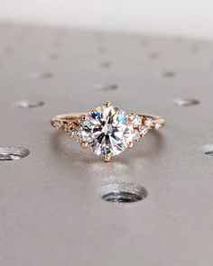 an engagement ring with three stones in the middle and two diamonds on each side, sitting on top of a metal surface