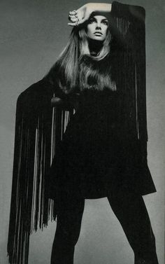 a black and white photo of a woman with long hair wearing a fringed coat