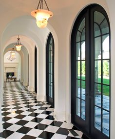 a hallway with black and white checkered flooring, arched doors and chandelier