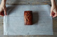 a loaf of bread sitting on top of a piece of paper next to two hands