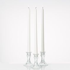 two white candles sitting next to each other in front of a white wall and floor