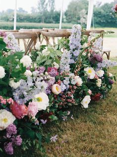 rows of flowers lined up along the side of a wooden bench at a wedding ceremony