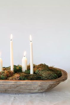 four white candles are lit in a moss covered bowl