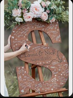 a wooden easel with writing on it and flowers in the top, as well as a handwritten wedding date