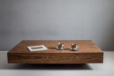 two silver cups sitting on top of a wooden table next to a book and magazine