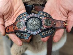 two hands holding a leather belt with an intricate design on the front and back,