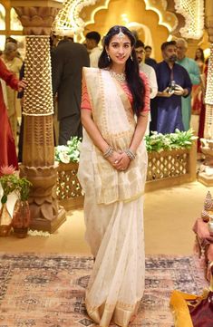 a woman in a white sari posing for the camera with other people behind her