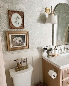 a white toilet sitting under a bathroom mirror next to a wooden sink vanity with two framed pictures on the wall