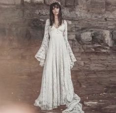 a woman wearing a white dress standing in front of a stone wall