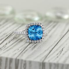 a ring with a blue topaz surrounded by white diamonds on a wooden surface,