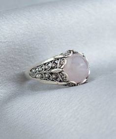 Elevate your style with this stunning Handmade Filigree Art Rose Quartz Gemstone Women Silver Cocktail Statement Ring. The 10mm cabochon round-cut Rose Quartz gemstone set in an elegant silver band measures 13.50mm in length and width, creating a beautiful contrast between the soft pink hues of the gemstone and the silver metal. Crafted with intricate details that showcase the beauty of filigree, an ancient art form originating from Mesopotamia and Anatolia, this exquisite ring is a true work of Elegant Adjustable Rose-colored Ring, Elegant Cabochon Rings, Elegant Silver Rings With Rose Design, Elegant Crystal Ring With Gemstone Accents, Elegant Cabochon Ring With Round Stone, Elegant Sterling Silver Ring With Rose Design, Rose Classic Formal Jewelry, Classic Rose-colored Formal Jewelry, Round Rose Design Jewelry For Anniversary