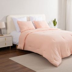 a bed with pink comforter and pillows in a bedroom