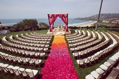 an outdoor ceremony set up with white chairs and pink flowers on the aisle, overlooking the ocean