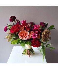 a bouquet of flowers sitting on top of a white table next to a gray wall