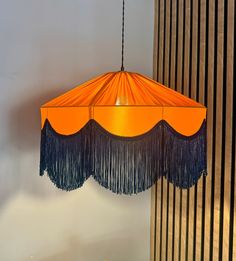 an orange and blue lamp shade hanging from a ceiling in a room with vertical blinds