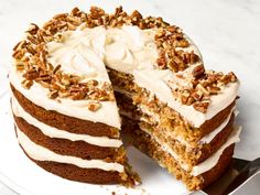 a large carrot cake with white frosting and pecans on top, cut in half