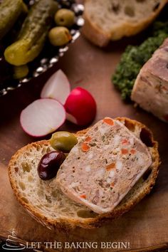 a piece of bread with meat, olives and pickles on it next to other food items