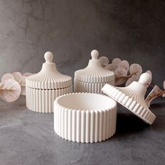 three white ceramic containers sitting next to each other on top of a gray countertop