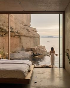 a woman standing in front of a bed looking out at the ocean from inside a bedroom