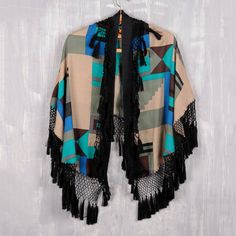 Cloak yourself in warmth and style wearing this bold wrap from India's Arnab Roy. Crafted from 100% wool, the wrap features a vivid geometric design screen printed in hues of ultramarine, turquoise, and beige. A black cotton macrame trim adorned with black tassels adds a playful yet elegant touch. Fall Multicolor Fringe Shawl, Black Bohemian Scarf For Fall, Bohemian Patterned Scarves For Fall, Black Bohemian Wraps For Winter, Bohemian Black Winter Wrap, Winter Bohemian Black Wrap, Bohemian Multicolor Wraps For Fall, Bohemian Multicolor Wrap For Fall, Bohemian Multicolor Fall Wraps