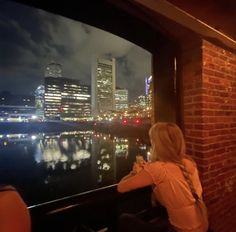 a woman is looking out at the city skyline from a restaurant in front of a river