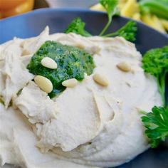 a blue plate topped with hummus, broccoli and cashew toppings