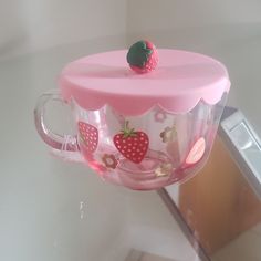 a pink tea cup with strawberries on the top is hanging from a hook in front of a mirror