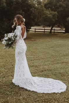 a woman in a white wedding dress standing on the grass with her back to the camera