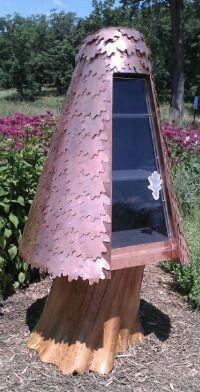 a wooden structure with a glass window in the middle of some grass and flowers behind it