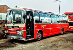 two red buses parked next to each other in front of a brick wall and building