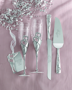 two champagne flutes, one filled with pearls and the other decorated with silverware on a pink table cloth