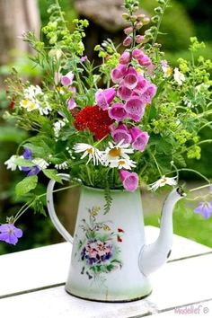 a pitcher filled with lots of flowers sitting on top of a wooden table next to grass