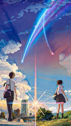 two people standing on a hill looking at the sky with a rainbow in the background