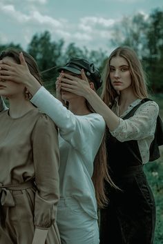 three young women standing next to each other with their hands covering their eyes and looking into the distance