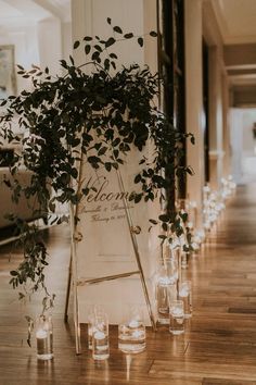 candles are lined up on the floor next to an easel with greenery in it