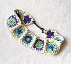 two crocheted headbands are laying on a white surface, one has blue and green flowers