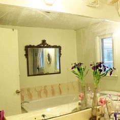 a bathroom with a sink, mirror and flowers in vases on the counter top