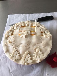 a cake that has been decorated with white frosting and christmas trees on it next to a knife