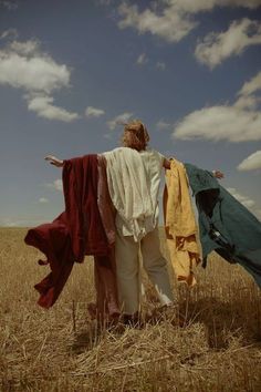 two women standing in a wheat field with their arms spread out to dry clothes on them