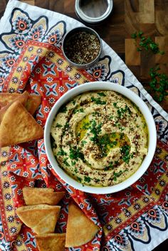 a bowl of hummus with pita chips on the side next to some dipping sauce