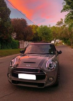 a car is parked on the side of the road in front of some trees at sunset