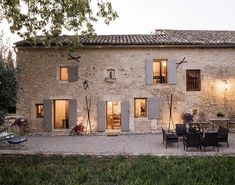 an old stone house with patio and dining table in the front yard at night time