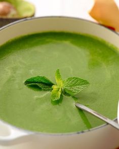 a bowl filled with green soup and topped with a leaf