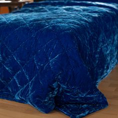 a blue bedspread on top of a wooden floor next to a table and chair