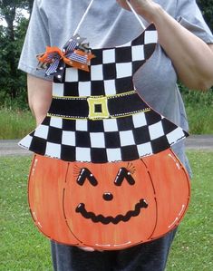 a woman is holding up a pumpkin shaped sign with a checkered hat on it's head