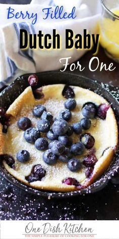 blueberry filled dutch baby in a cast iron skillet with text overlay that reads, berry filled dutch baby for one