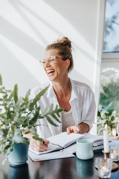 a woman sitting at a table with a book and plant in front of her smiling