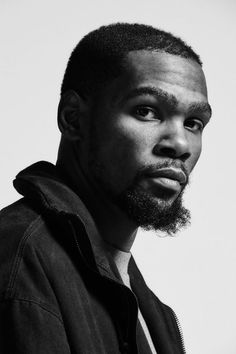 a black and white photo of a man with a beard looking at the camera while wearing a jacket