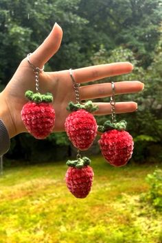 the hand is holding four small strawberries on chains hanging from it's fingers